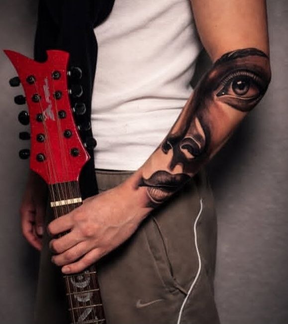 Color realism forearm tattoo of face with eye and guitar